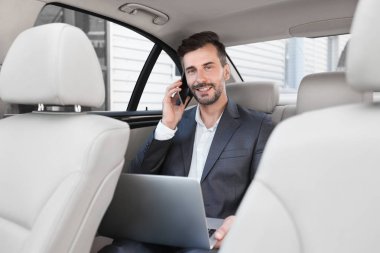 Otomobillerde geri oturan dizüstü bilgisayar üzerinde çalışan iş adamı