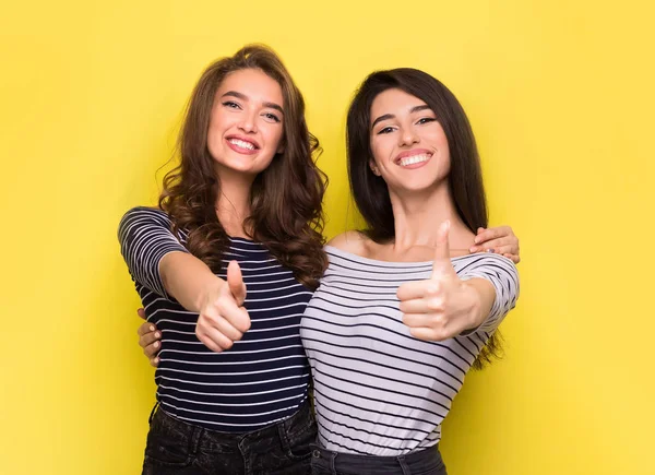 Lindas mujeres amigas mostrando pulgares hacia arriba sobre fondo amarillo —  Fotos de Stock