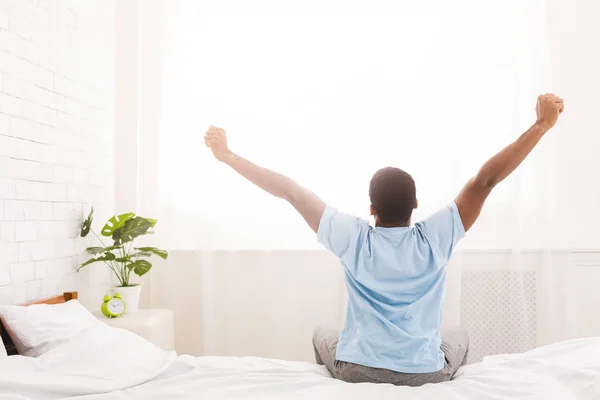 Junger Mann wacht im Bett auf und streckt die Arme aus — Stockfoto