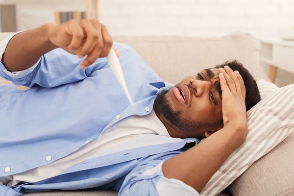 Hombre negro enfermo comprobando su temperatura en casa — Foto de Stock