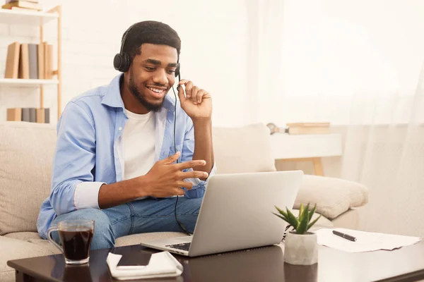 微笑的非洲裔美国人的家伙在耳机看着笔记本电脑 — 图库照片