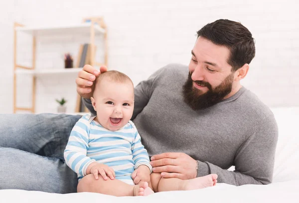 Young bearded man playing with his little baby in bed — Stock Photo, Image