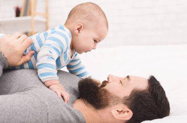 Dad and son connection. Adorable baby looking into father eyes, lying on his chest clipart