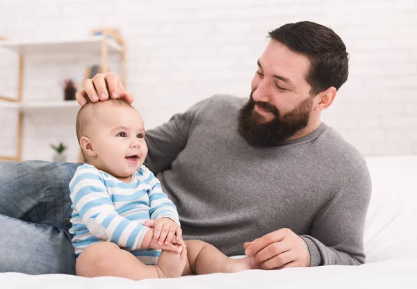 Jovem barbudo brincando com seu bebê na cama — Fotografia de Stock