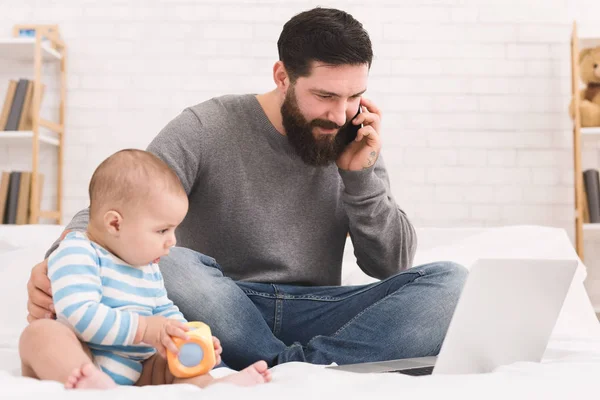 Young dad working on laptop at home with his baby son — Stock Photo, Image