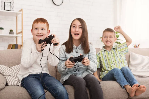 Hermanos jugando a la consola de juegos mientras el niño los anima —  Fotos de Stock