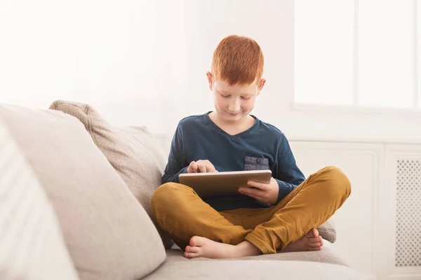 Мальчик играет в игры на цифровом планшете на диване — стоковое фото
