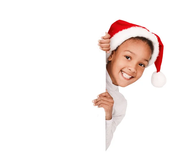 Menina afro-americana espreitando sobre placa em branco, vestindo chapéu de Papai Noel — Fotografia de Stock