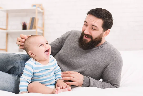 Jovem barbudo brincando com seu bebê na cama — Fotografia de Stock