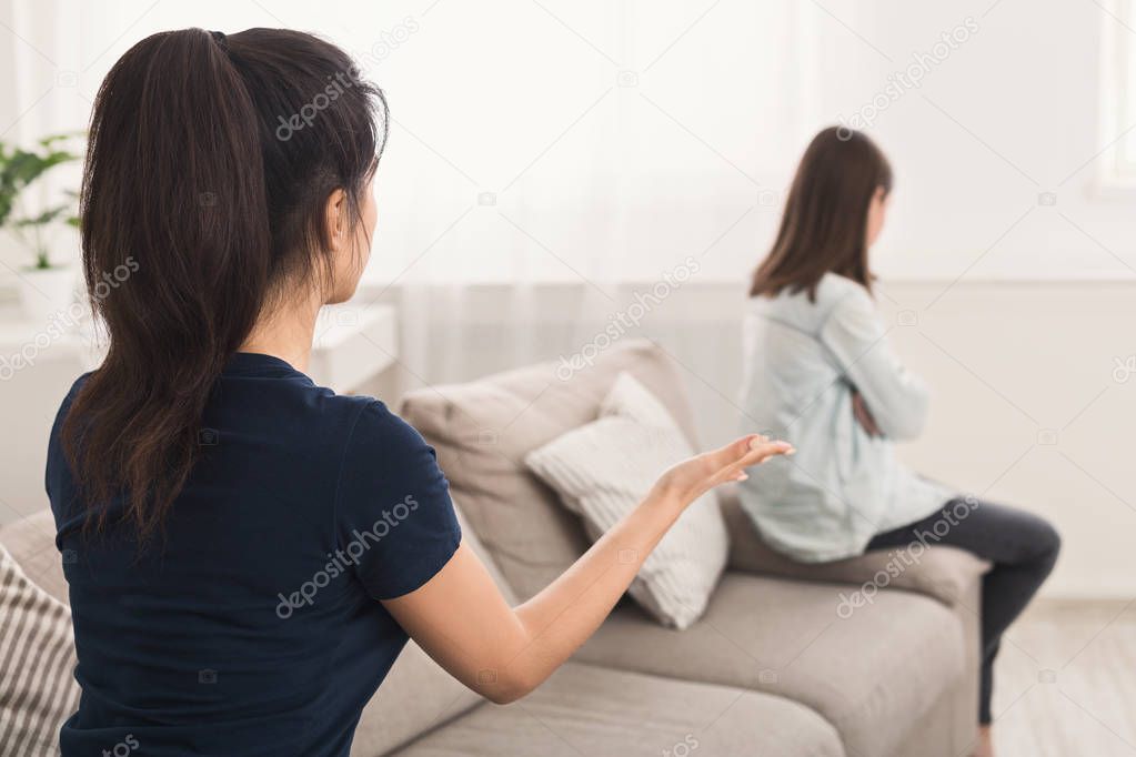 Mother looking at daughter who sitting sadly on sofa