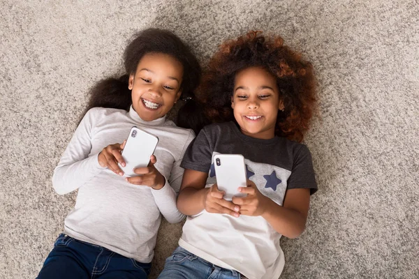 Chicas felices con teléfonos inteligentes tumbados en el suelo — Foto de Stock