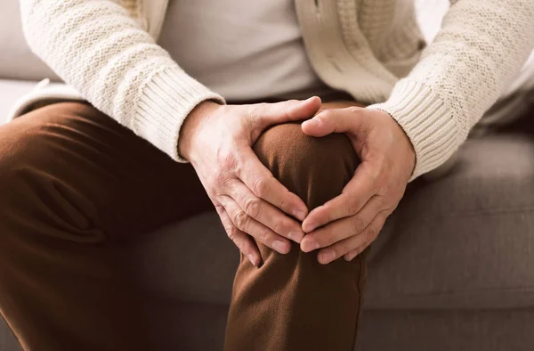 Uomo maturo che soffre di dolore al ginocchio sul divano — Foto Stock