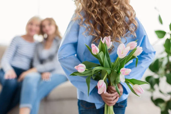 Linda chica adolescente escondiendo flores para su abuela y madre —  Fotos de Stock