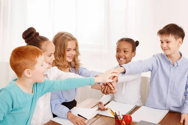 Children putting their hands together in classroom — Stock Photo, Image