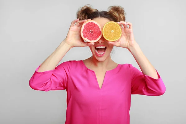 Mulher brincalhão segurando metades de frutas cítricas, cobrindo os olhos — Fotografia de Stock