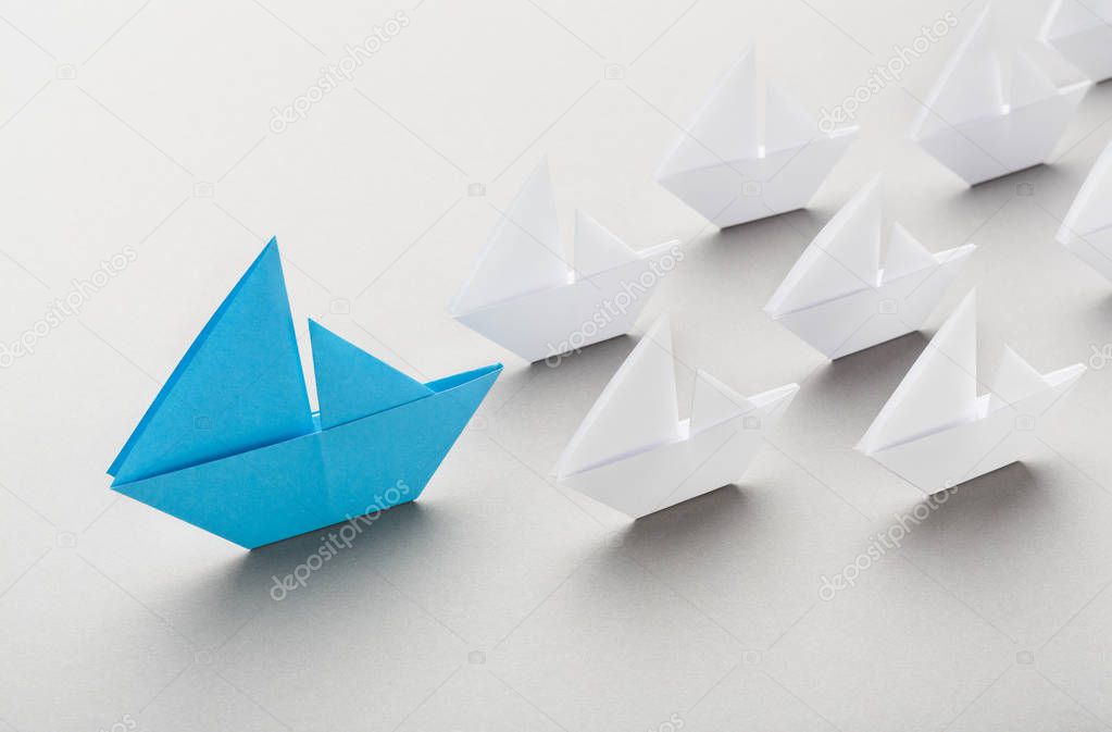 Blue paper boat leading among white ships
