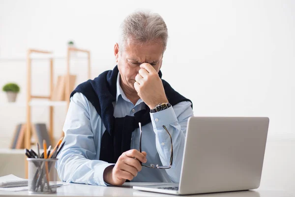 Виснажений зрілий чоловік, що працює на ноутбуці, відчуває втому — стокове фото