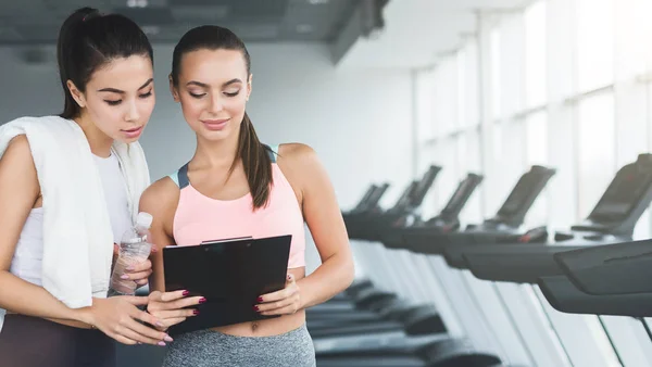 Fitness instructor showing exercise plan to woman — Stock Photo, Image