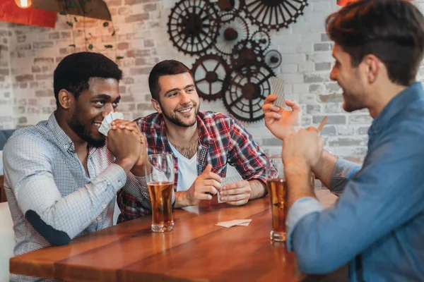 Hombres multiculturales jugando a las cartas, descansando en el bar — Foto de Stock