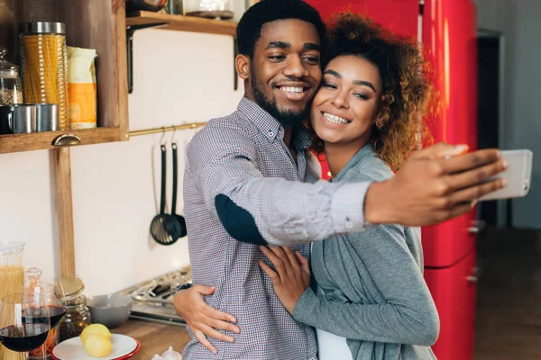 Αφρικανικός-αμερικανική ζευγάρι λαμβάνοντας αυτοπορτρέτα στο smartphone στην κουζίνα — Φωτογραφία Αρχείου