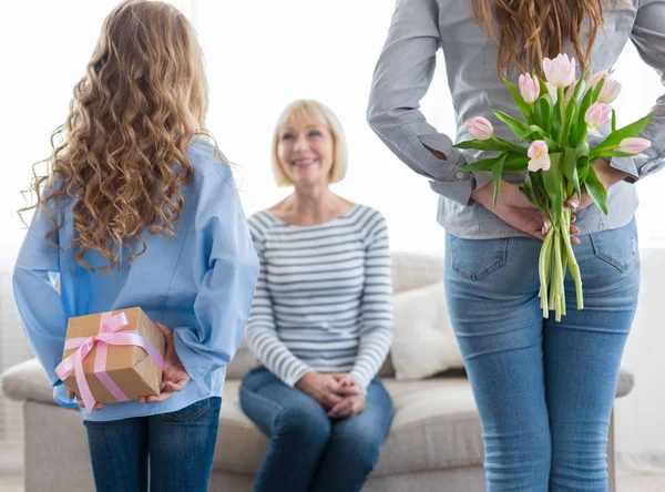 Chica y su mamá ocultando flores y caja de regalo para la abuela —  Fotos de Stock
