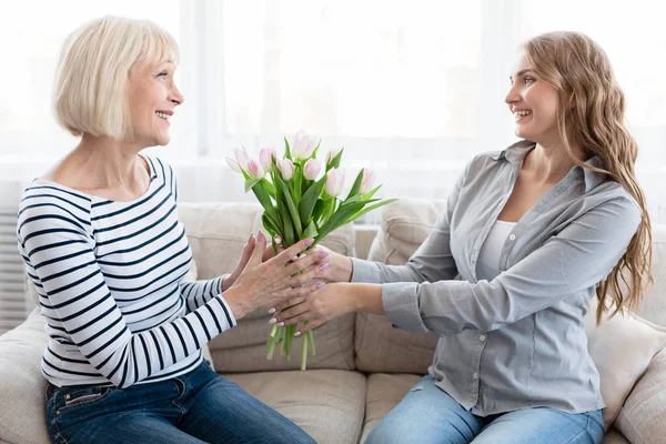 Frau überreicht Tulpenstrauß an Seniorin — Stockfoto