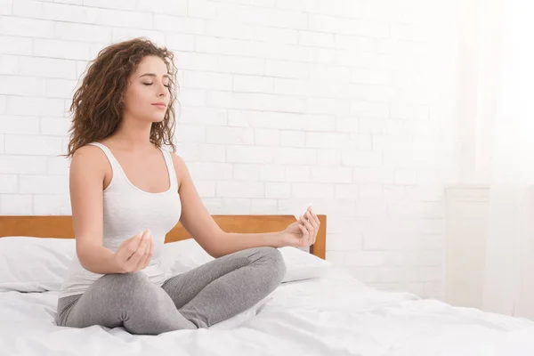 Jovem mulher meditando na posição de lótus na cama — Fotografia de Stock