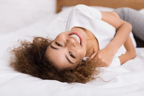 Donna felice sdraiata sul letto e guardando la fotocamera — Foto Stock