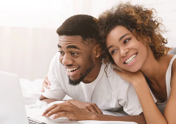 Junges schwarzes Paar liegt auf Bett und benutzt Laptop. — Stockfoto