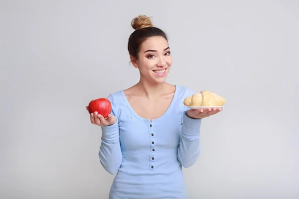 Genç kadın kruvasan ve elma arasında seçim yapma — Stok fotoğraf