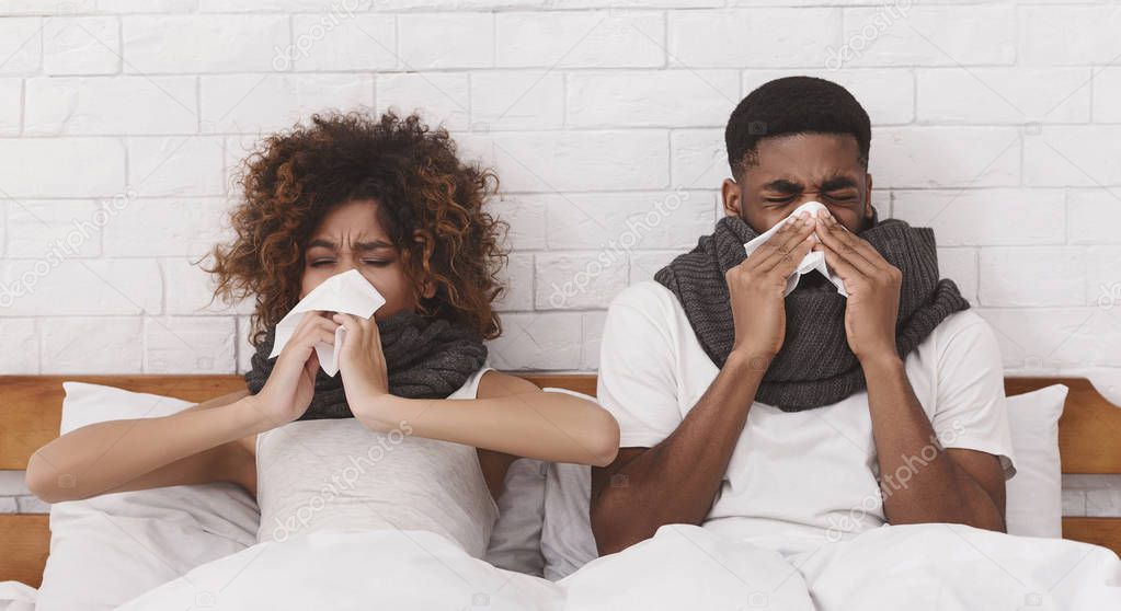 Sick african-american couple blowing noses in bed