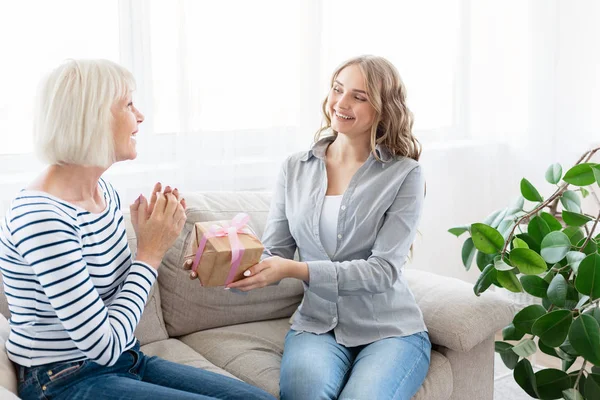 Genç bir kadın, büyük annesini hediye kutusuyla tebrik ediyor.