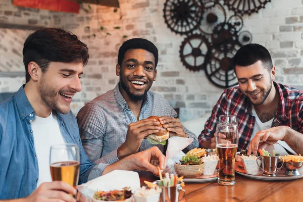 Üç adam hamburger ve bira zevk içinde bar — Stok fotoğraf