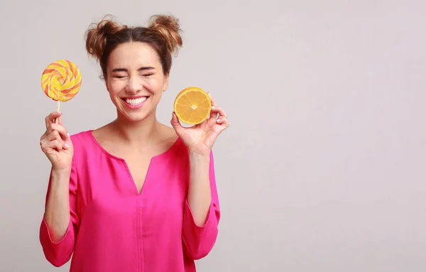 Mujer feliz con piruleta y naranja sobre fondo —  Fotos de Stock