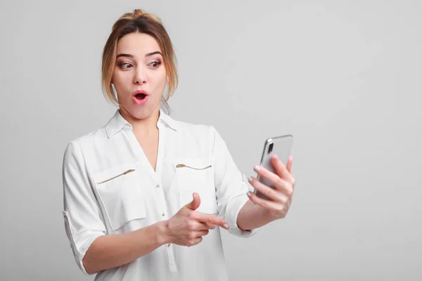 Verrast vrouw kijken naar smartphone tegen de grijze achtergrond — Stockfoto