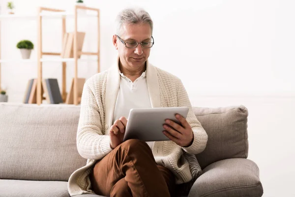 Hombre maduro leyendo noticias en la tableta en casa — Foto de Stock