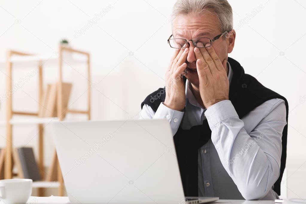 Hard day. Elderly man feeling tired, working on laptop