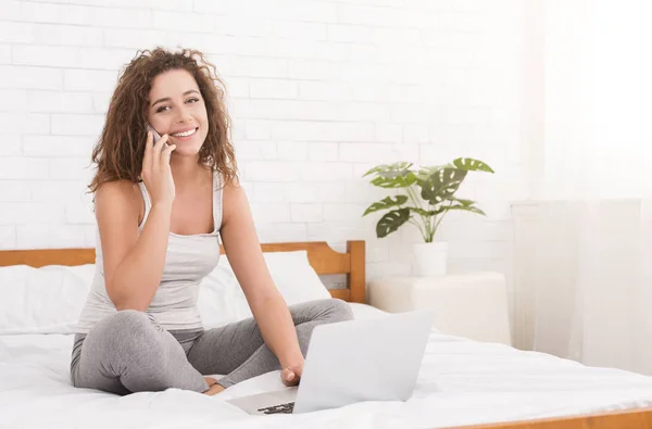 Mulher sentada na cama, trabalhando no laptop e chamando — Fotografia de Stock