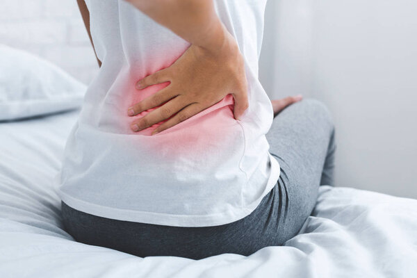 Woman suffering from back pain, sitting on bed