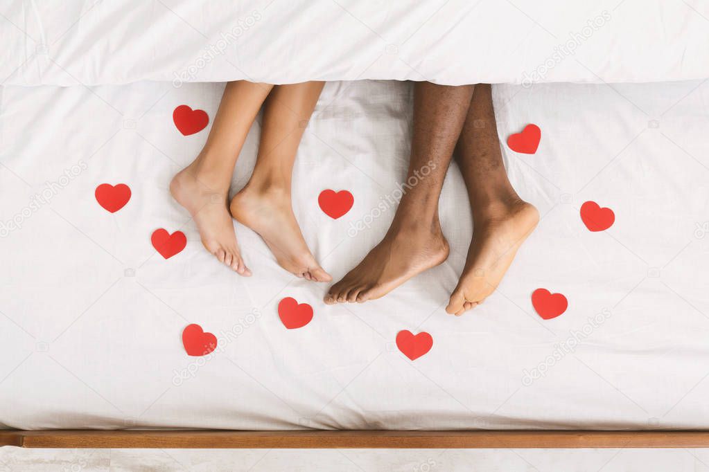 Loving couple legs lying on bed under blanket