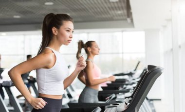Koşu bandı üzerinde çalışan kadınlar kardiyo yaparak spor salonunda egzersiz