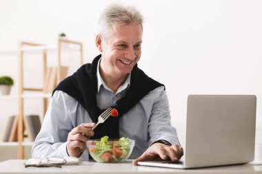 Salata yiyor ve dizüstü bilgisayarda olgun işadamı