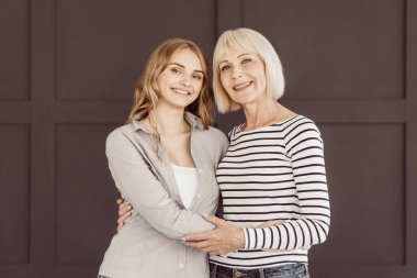 Mutlu anne ve kızı kameraya kahverengi duvardan arıyorsunuz