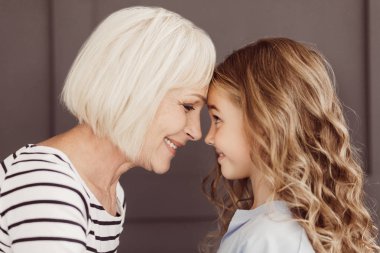 Büyükanne ve torunu dokunmadan kendi alınlarına, yan görünüm