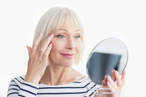 Glückliche Seniorin, die Augencreme gegen Falten aufträgt — Stockfoto