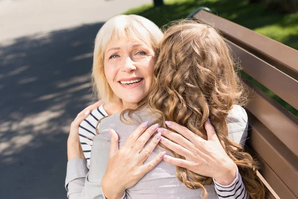 Åldriga mor omfamnar med dotter i park — Stockfoto