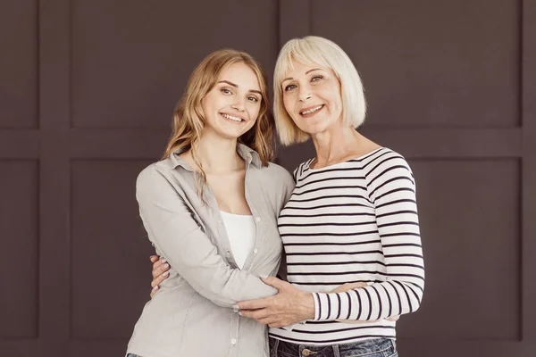 Happy mom and daughter looking at camera over brown wall — Stock Photo, Image