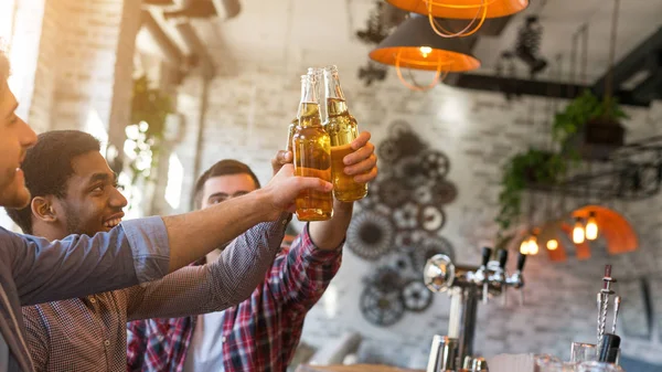 Friends having rest in bar, clinking beer bottles