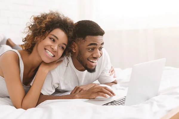 Молода чорна пара лежить на ліжку і використовує ноутбук . — стокове фото
