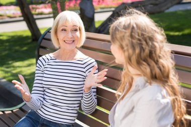 Mutlu kıdemli anne ve kızı bankta oturan